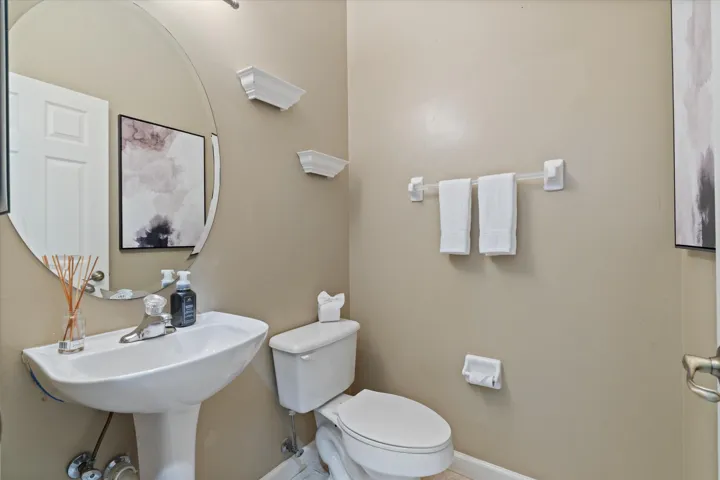 Pedestal sink, wall-mounted mirror, white toilet, and neutral wall paint
