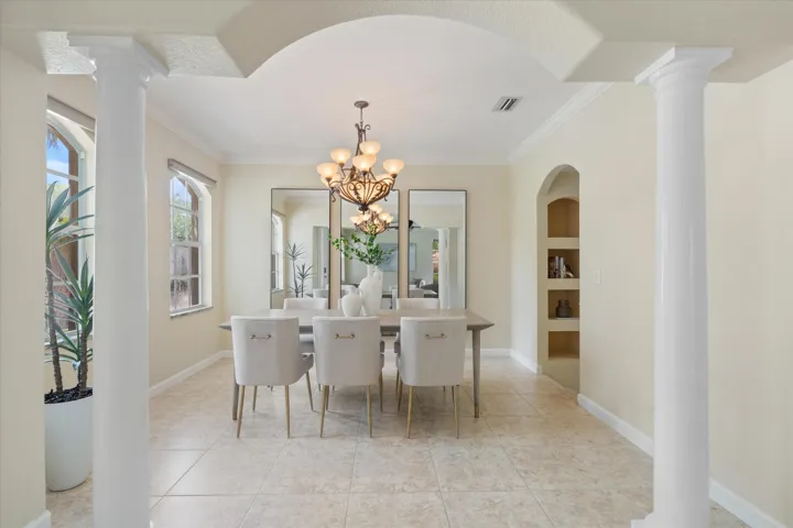 Arched entryway with decorative columns, tiled flooring, built-in shelving, and a chandelier