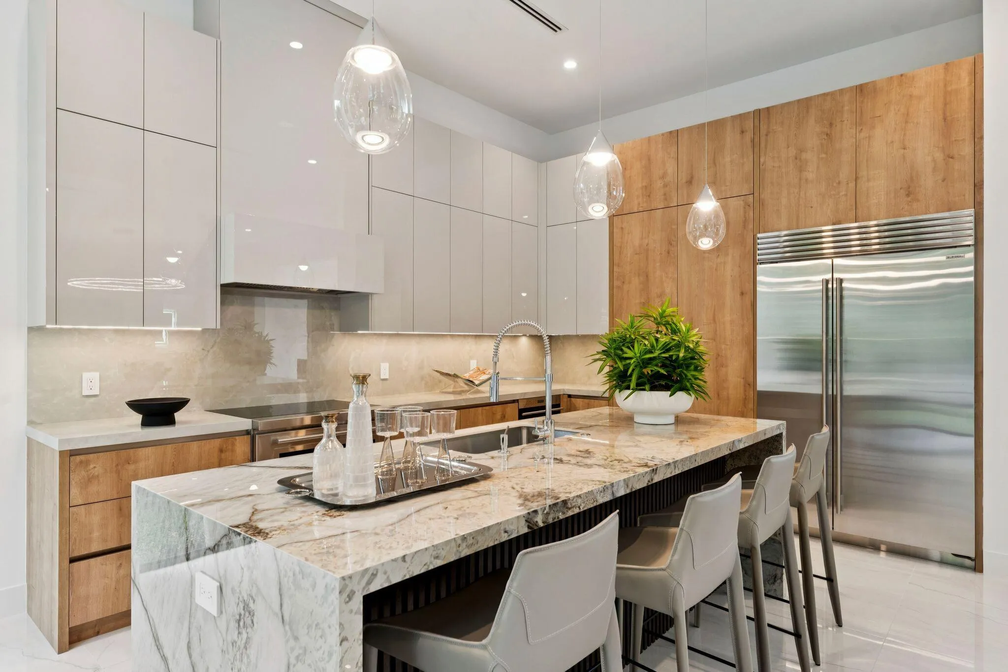 Waterfall island with integrated seating, stainless steel refrigerator, gloss white cabinetry, wood-finish accent cabinetry, and pendant lighting