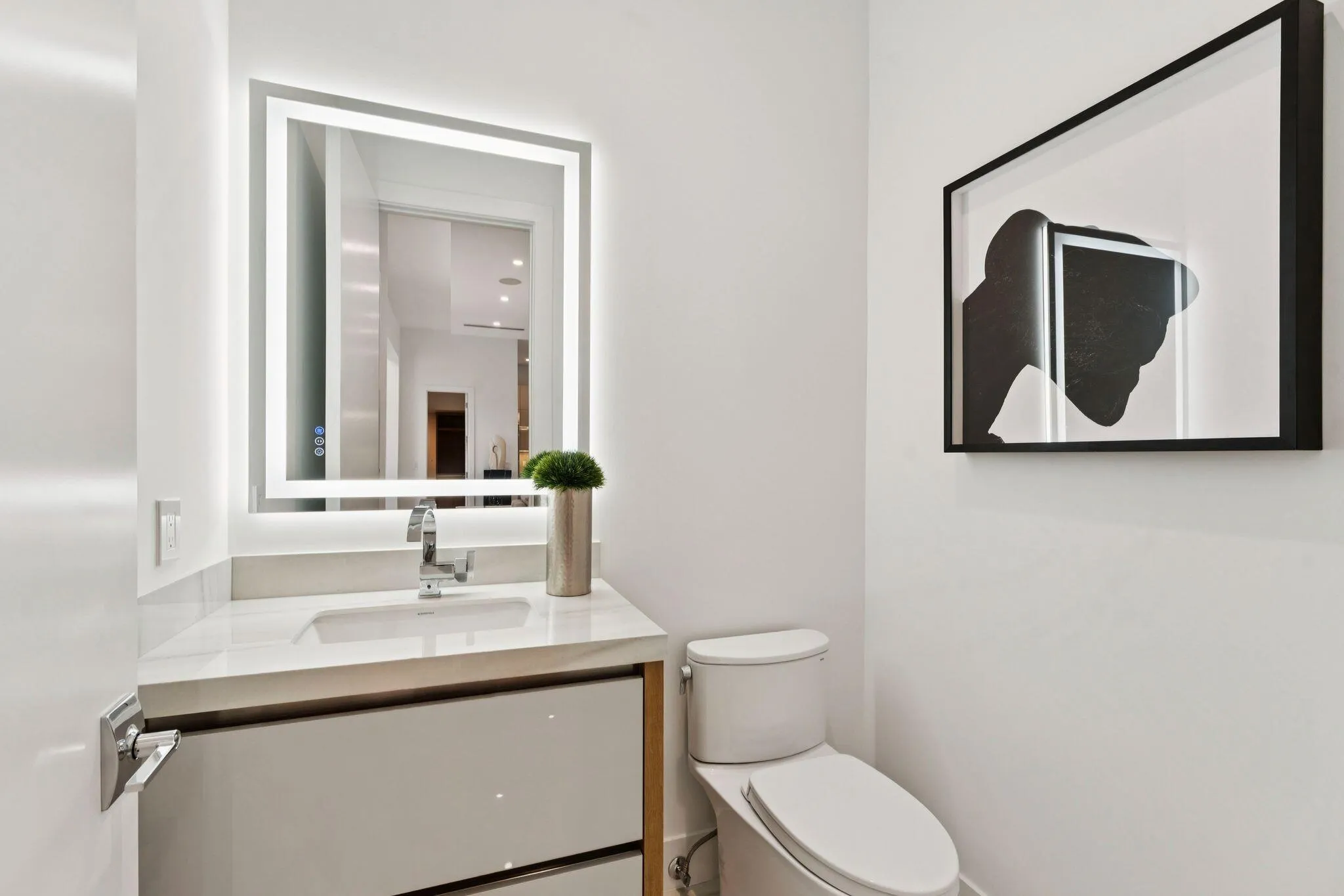 Modern vanity with an integrated sink, polished chrome faucet, illuminated mirror, and a contemporary toilet