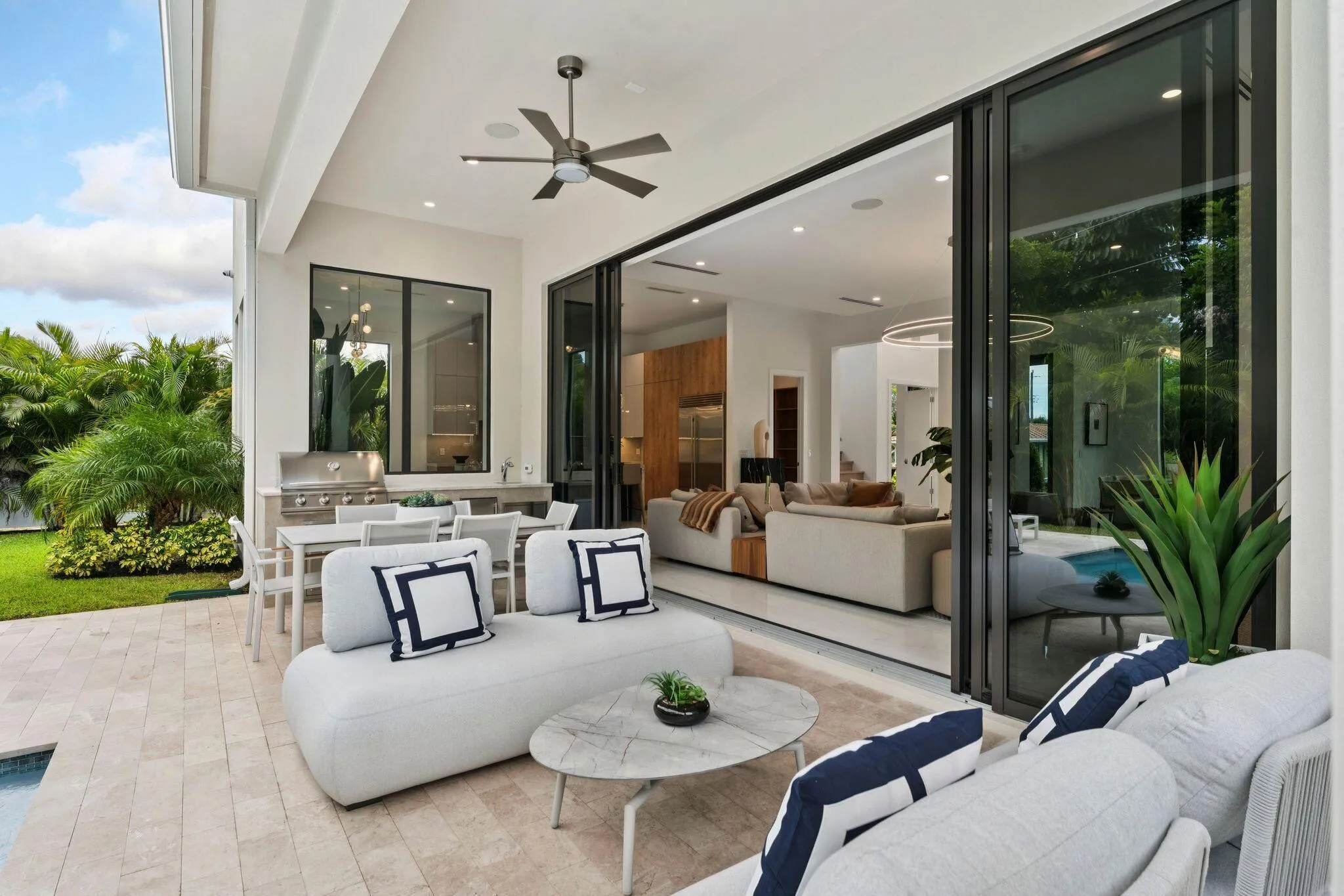 Expansive outdoor living area featuring a covered patio, built-in outdoor kitchen with grill, ceiling fan, and large sliding glass doors