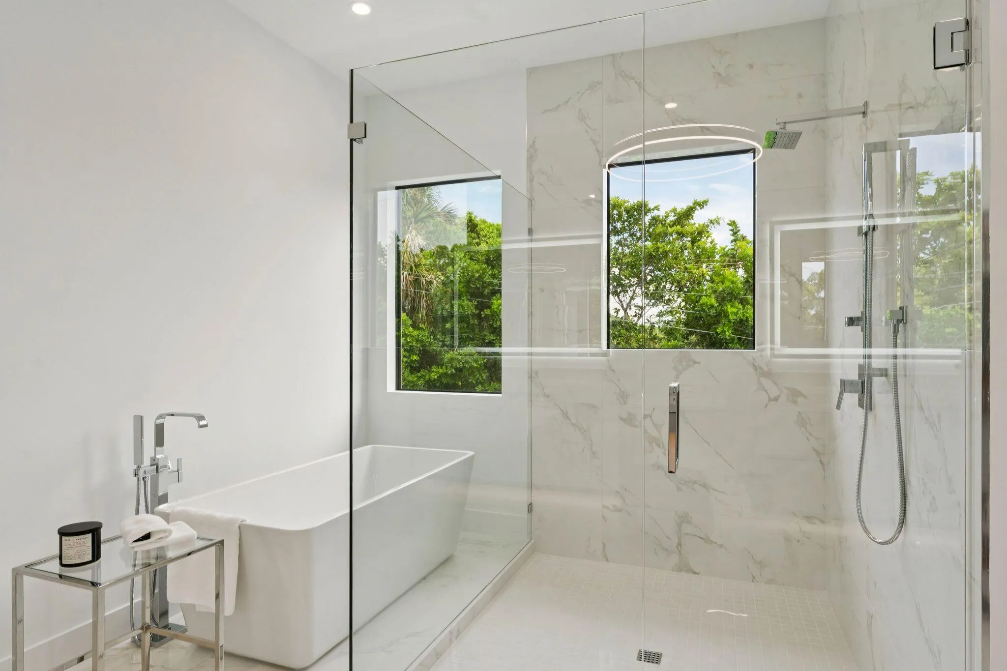 Freestanding soaking tub with a floor-mounted faucet, glass-enclosed shower, and large format wall tiling
