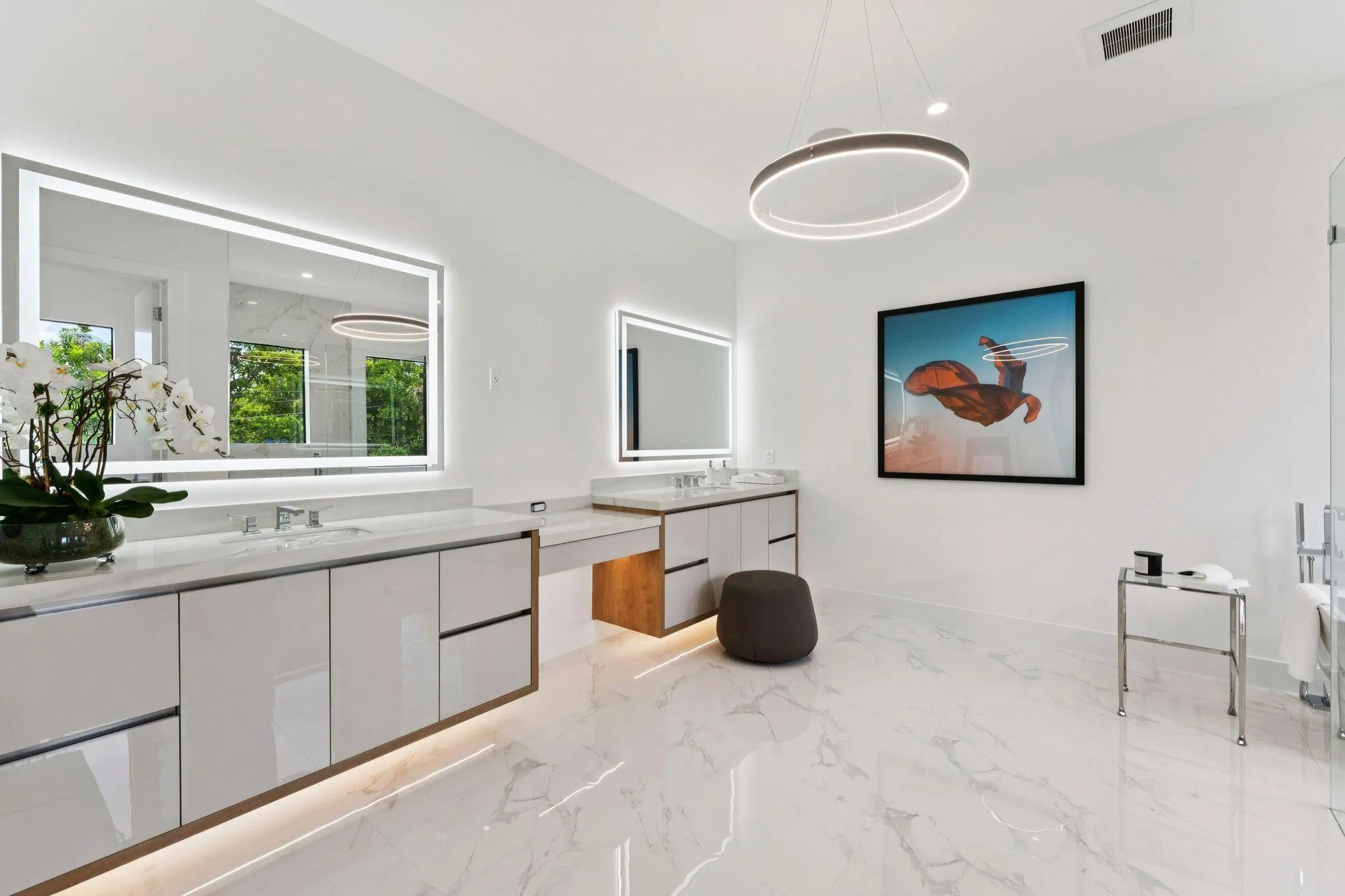 White marble-look flooring, dual vanity with undermount sinks and quartz countertops, back-lit mirrors, vanity lighting, and modern ring chandelier