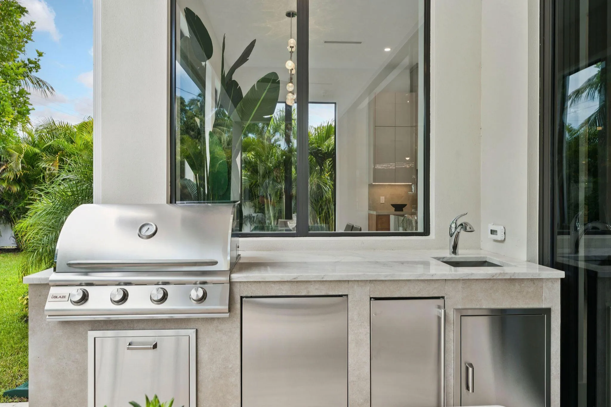 Outdoor kitchen featuring a built-in stainless steel grill, integrated stainless steel appliances, stone countertop, undermount sink, and modern black-framed windows