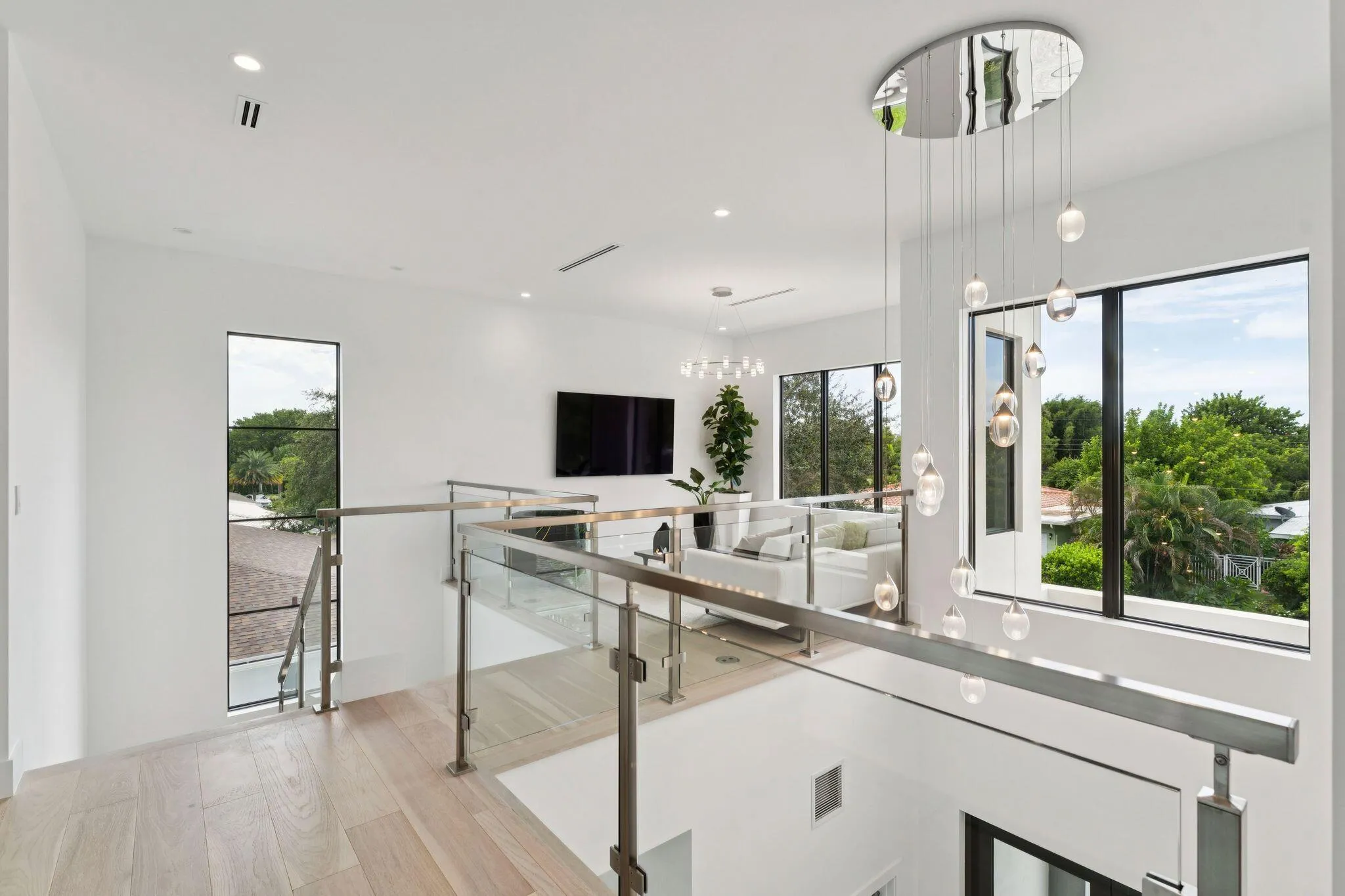 Light wood-finish flooring, glass and stainless steel railing, contemporary suspended lighting fixture, recessed ceiling lighting, and large windows