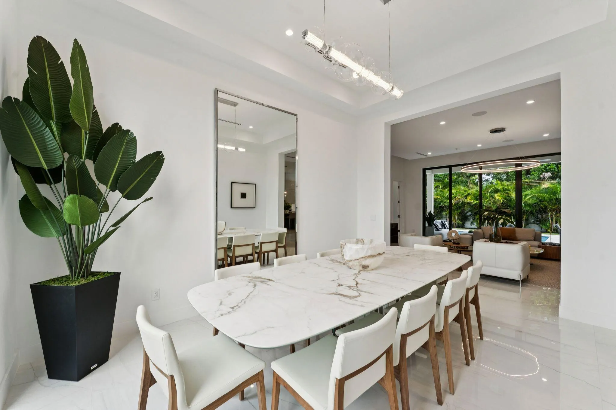 Open-concept dining area with a linear chandelier, large mirrored wall, and tile flooring