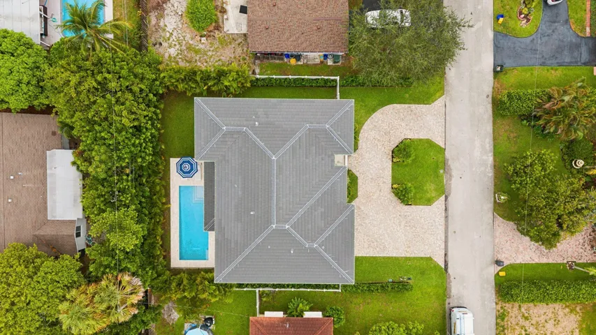 Expansive outdoor space featuring a swimming pool, mature perimeter landscaping, manicured lawn, and a patterned paver driveway