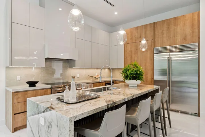 Waterfall island with integrated seating, stainless steel refrigerator, gloss white cabinetry, wood-finish accent cabinetry, and pendant lighting