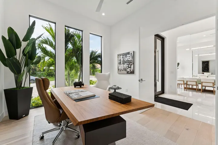 White walls with three tall windows, light wood-finish flooring, recessed lighting, and a modern glass entry door