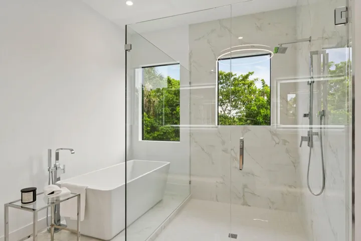 Freestanding soaking tub with a floor-mounted faucet, glass-enclosed shower, and large format wall tiling