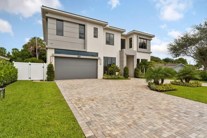 Contemporary two-story exterior with an attached garage, paver driveway, and a white privacy fence