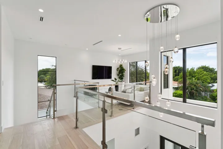 Light wood-finish flooring, glass and stainless steel railing, contemporary suspended lighting fixture, recessed ceiling lighting, and large windows