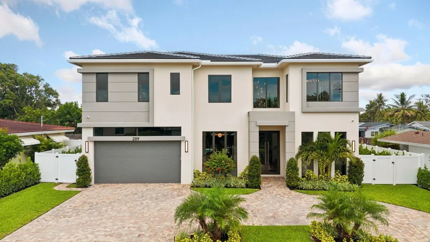 Two-story stucco facade, paver driveway, integrated garage, formal entry, and manicured landscaping