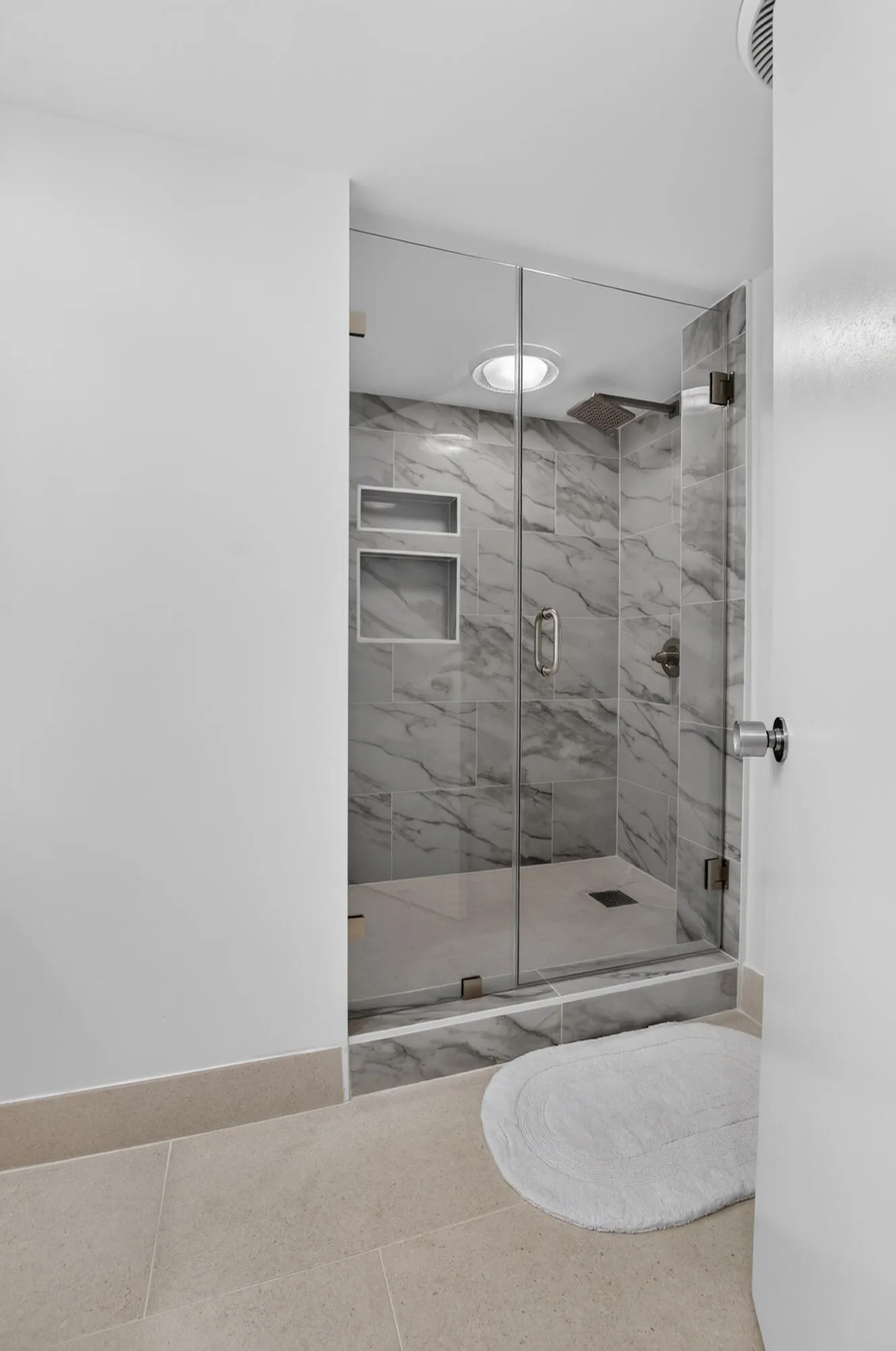 Glass-enclosed shower with marble-style tile surround, integrated shower niches, and an overhead light fixture