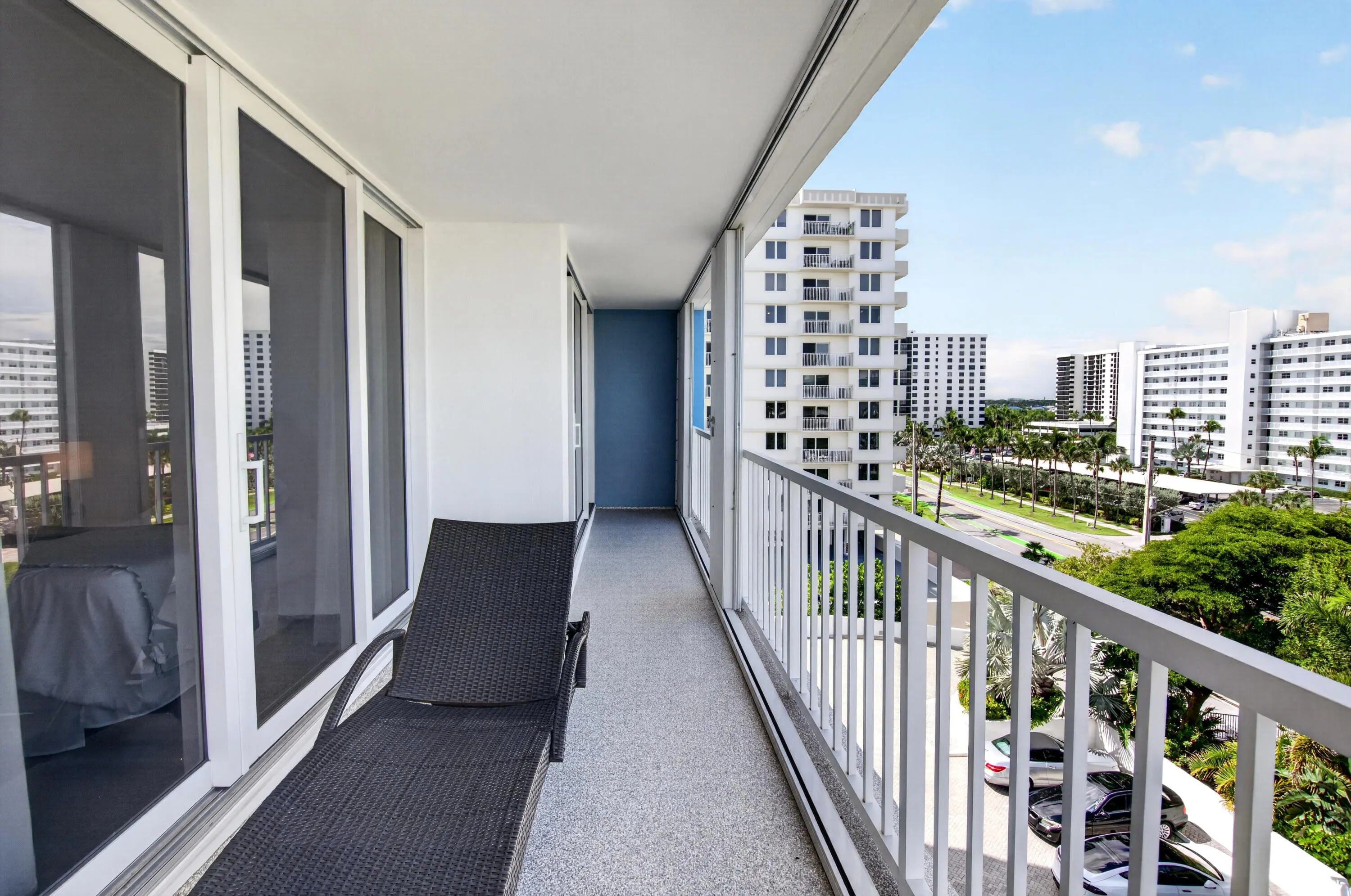 Outdoor balcony with white railings, textured flooring, and large sliding glass panels