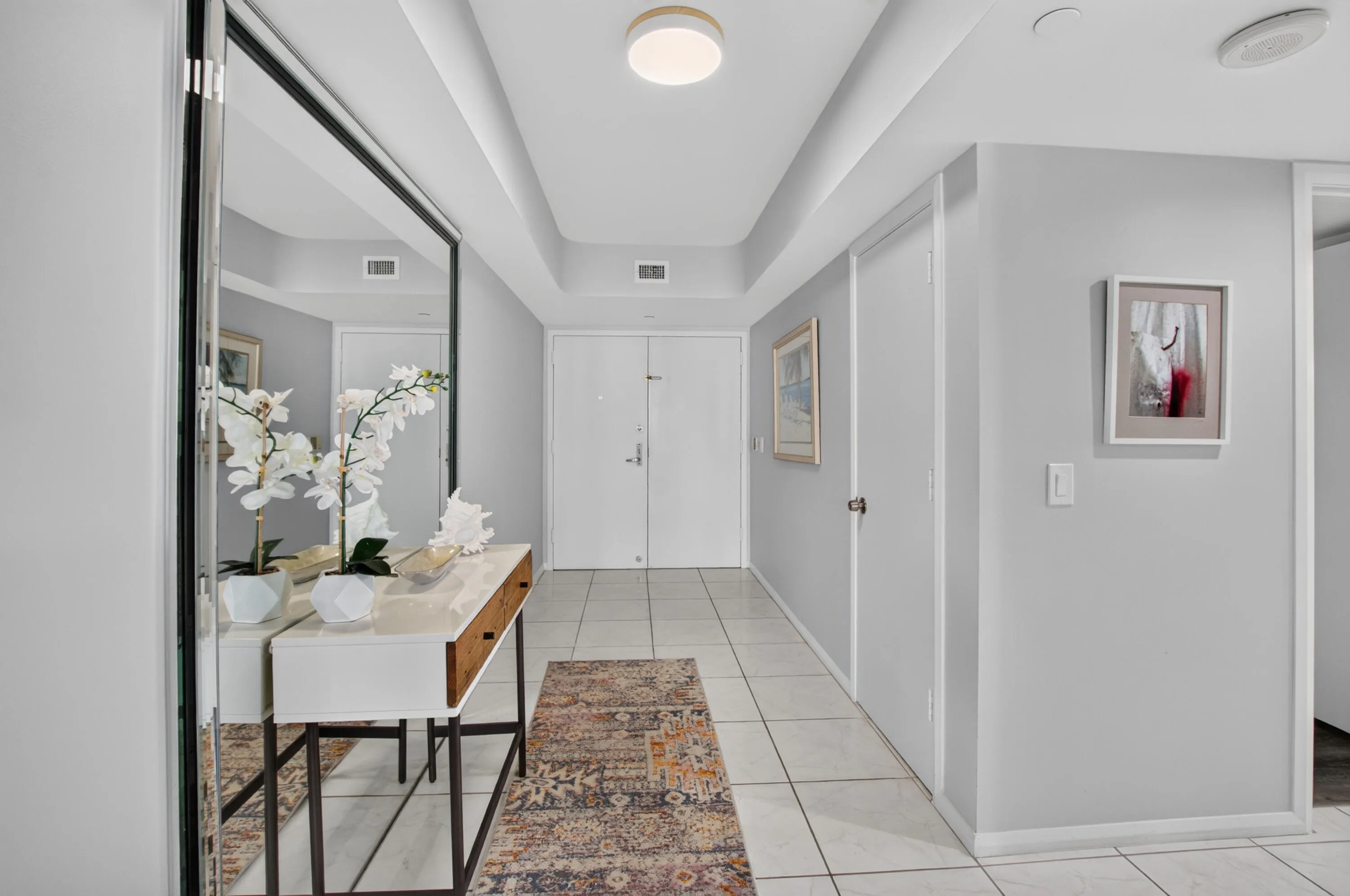 Recessed tray ceiling, ceramic tile flooring, double entry doors, wall-mounted light fixture, and a full-length mirror