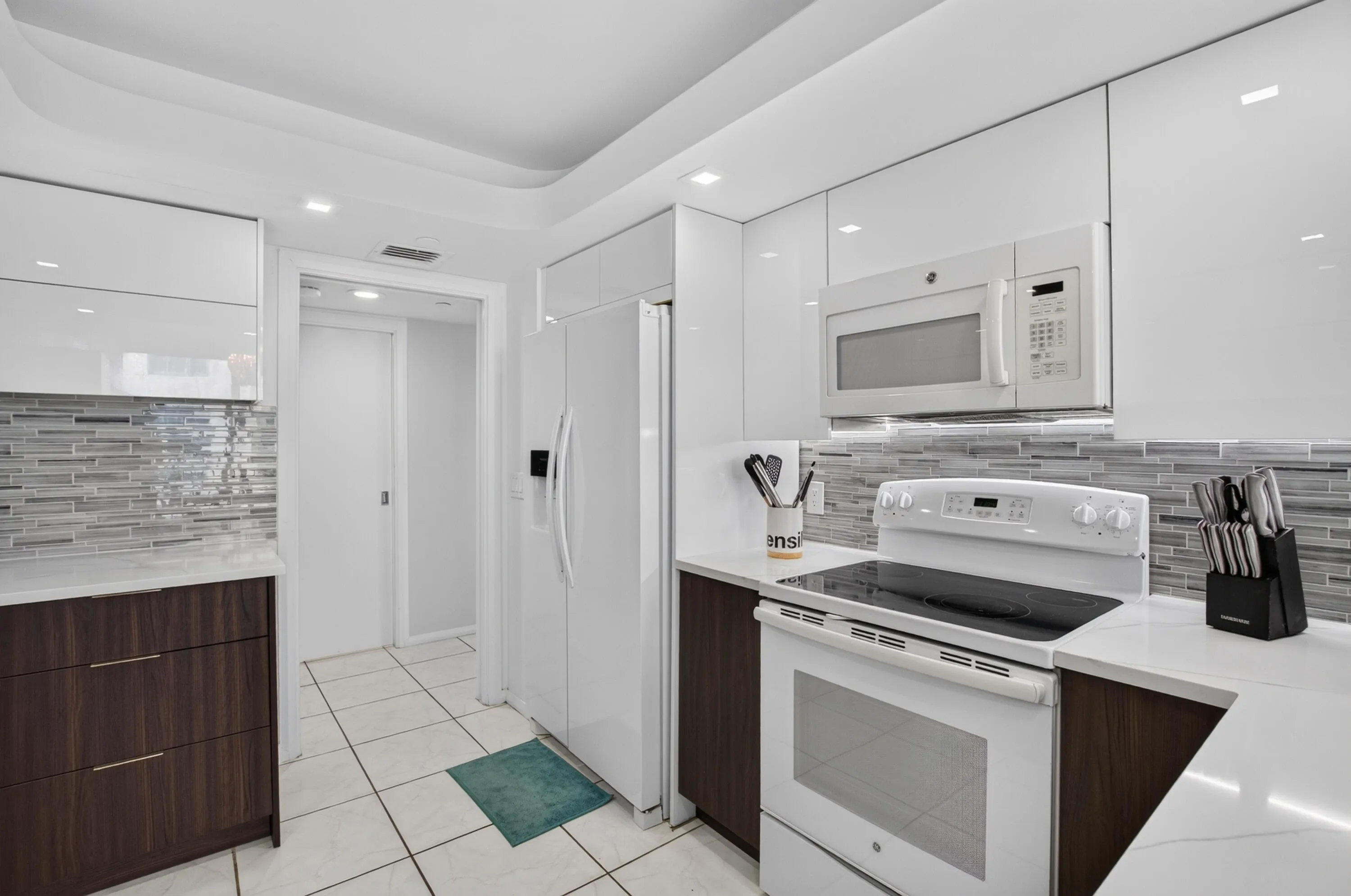 White flat-panel cabinetry, wood-finish lower cabinetry, white appliances, and a tiled backsplash