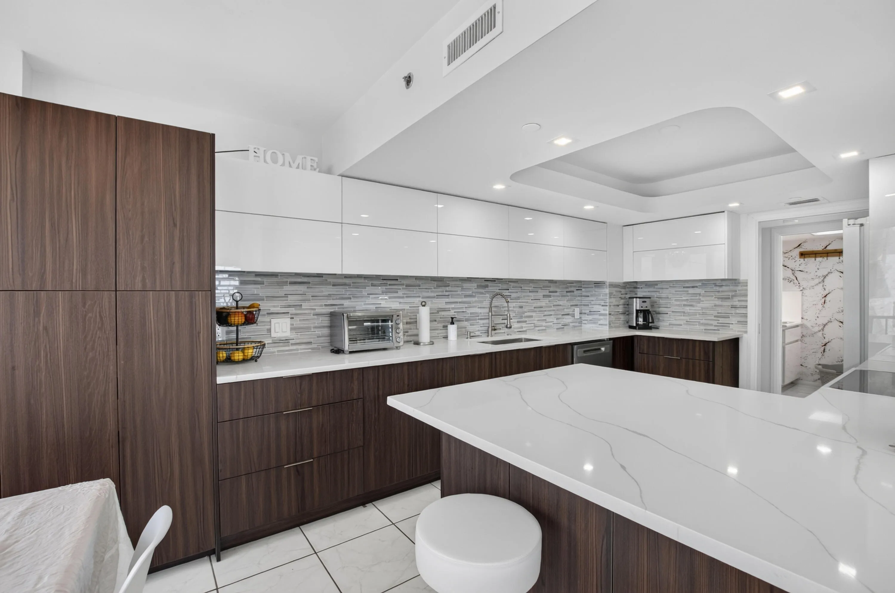 Kitchen featuring wood-finish lower cabinetry, white upper cabinetry, a patterned tile backsplash, and an island with a white countertop