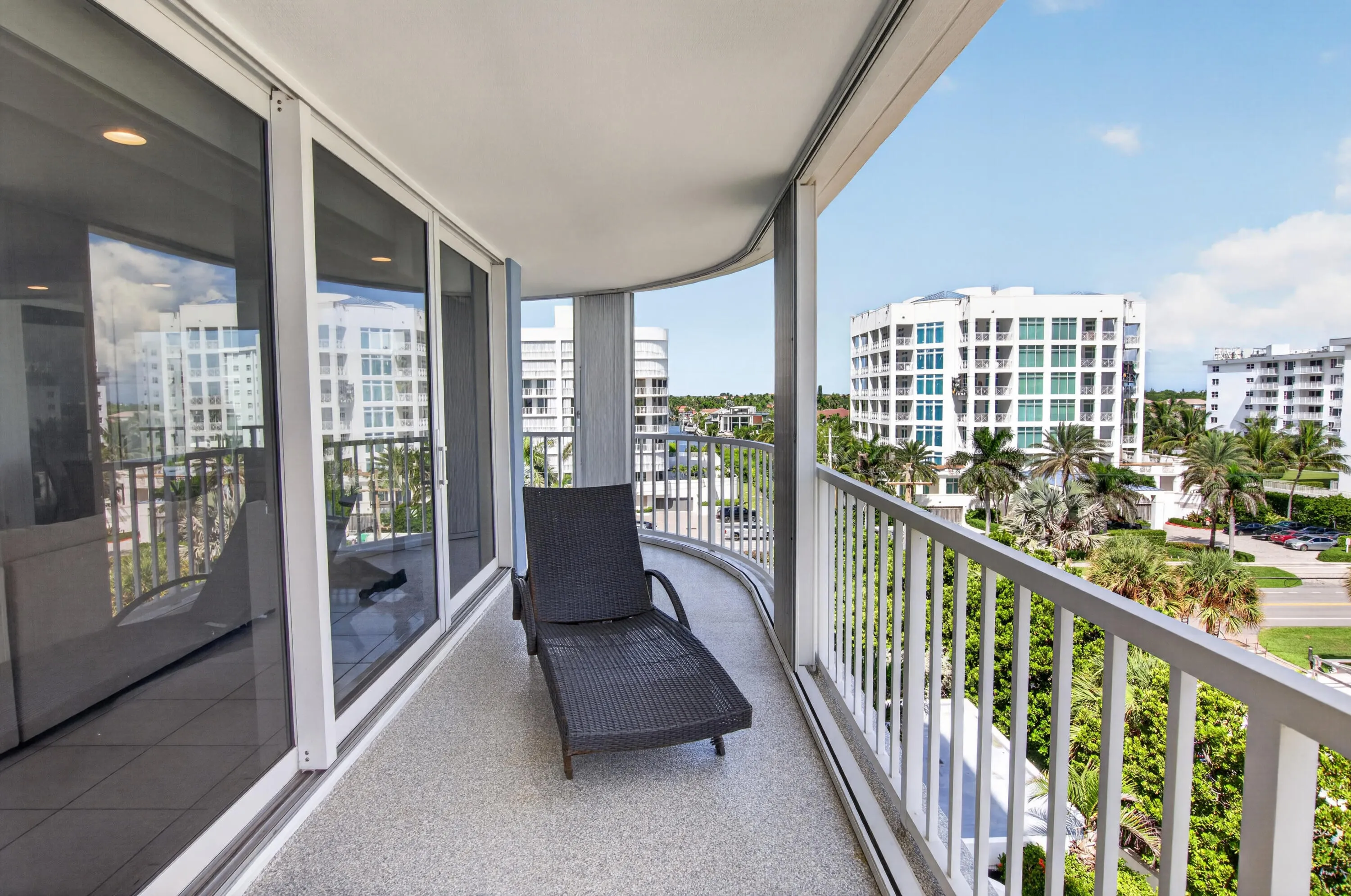 Curved balcony with white railing, textured flooring, and sliding glass doors