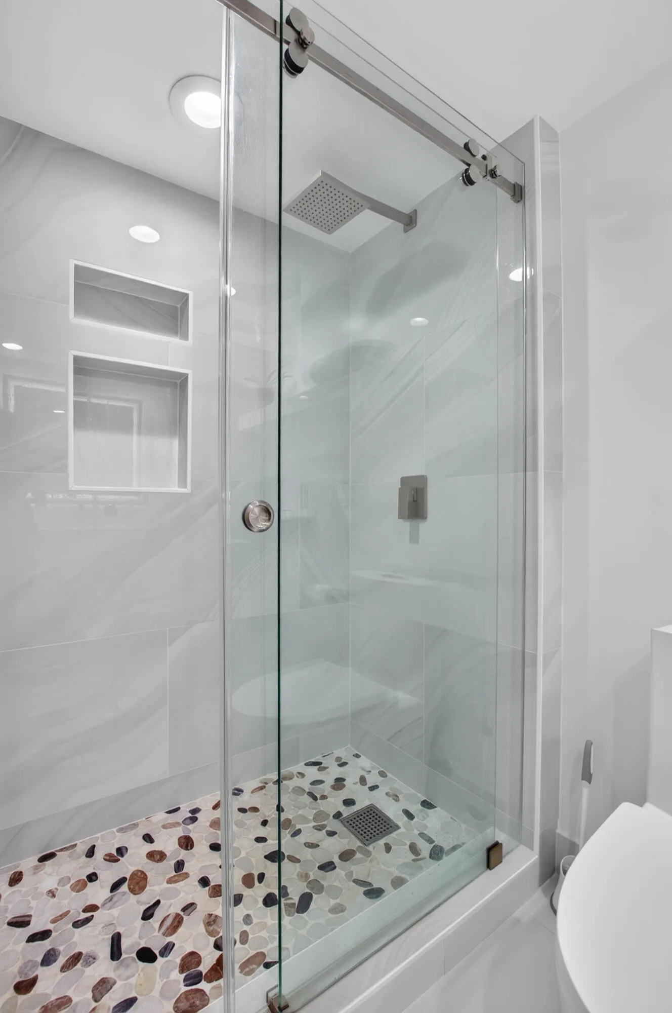 Glass-enclosed shower with a river rock floor, built-in bench, recessed wall niches, and a rainfall showerhead