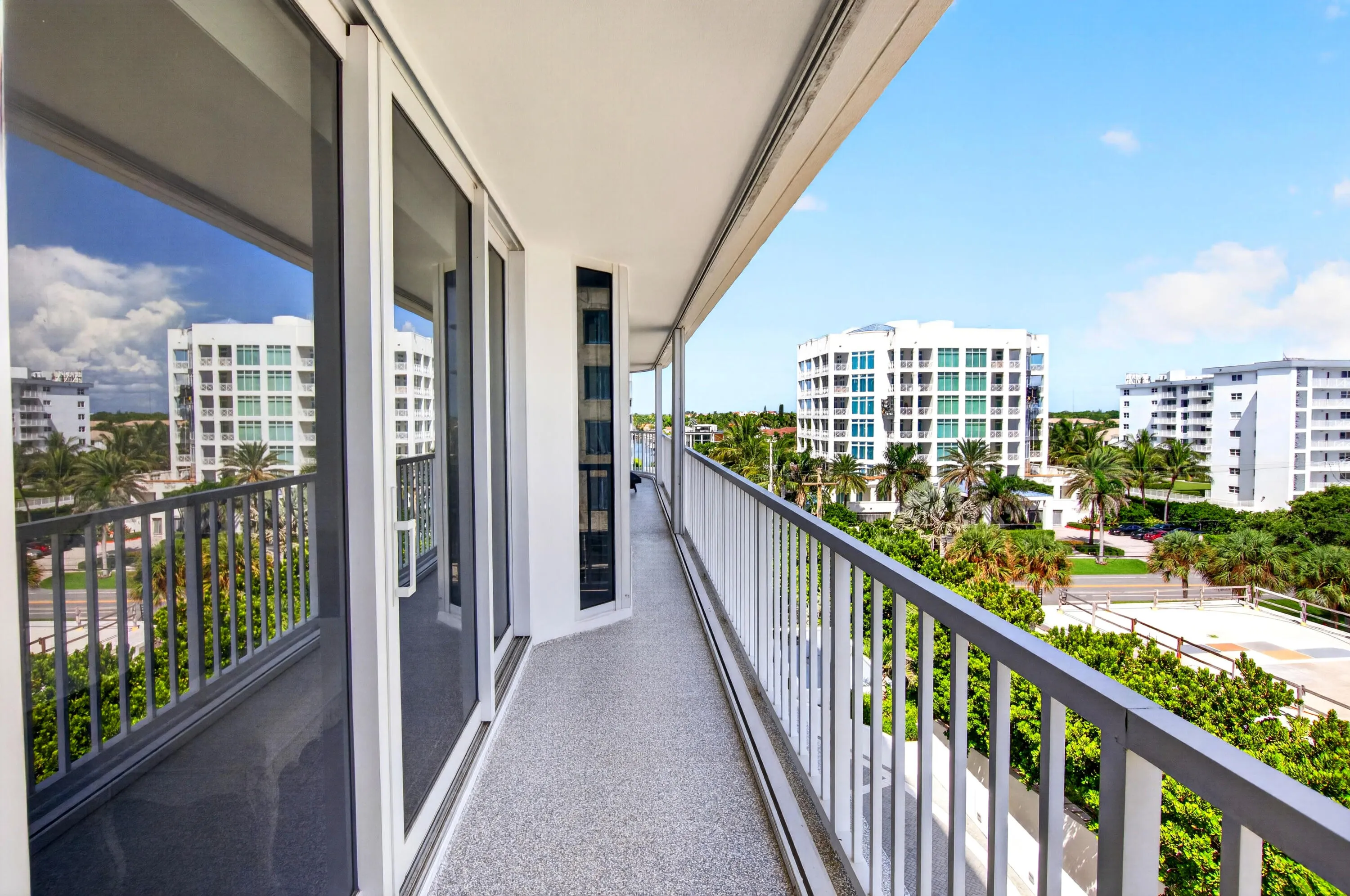 Expansive balcony featuring a textured flooring surface, white metal railing, and multiple sliding glass doors