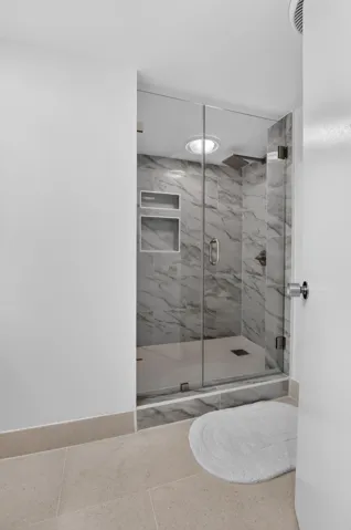 Glass-enclosed shower with marble-style tile surround, integrated shower niches, and an overhead light fixture