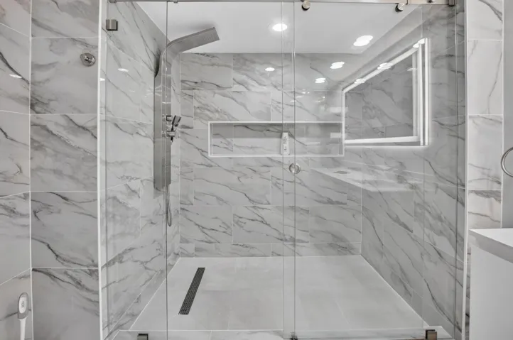 Glass-enclosed shower with full-height marble-look tile, linear drain, recessed lighting, and a built-in shower niche