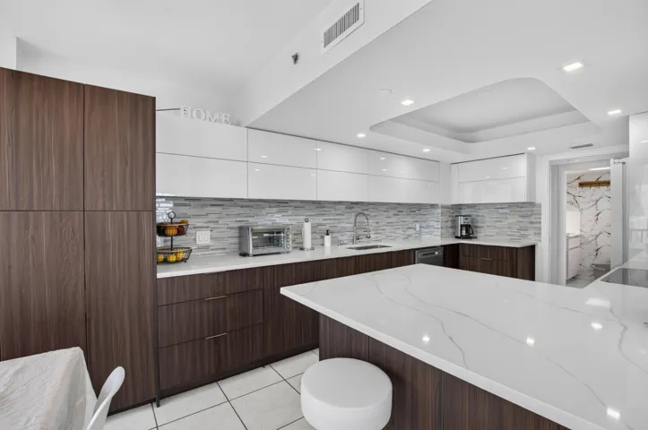 Kitchen featuring wood-finish lower cabinetry, white upper cabinetry, a patterned tile backsplash, and an island with a white countertop