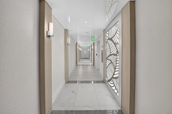 Corridor featuring sconce lighting, decorative wall panels, and high-gloss ceiling