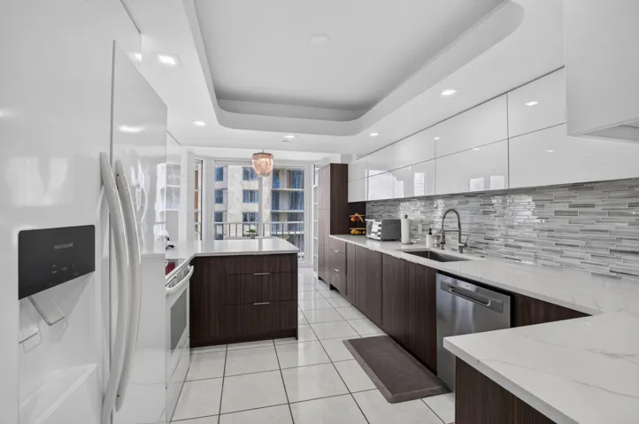 Modern kitchen featuring white glossy upper cabinetry, dark wood-finish lower cabinetry, white quartz countertops, and a tiled backsplash