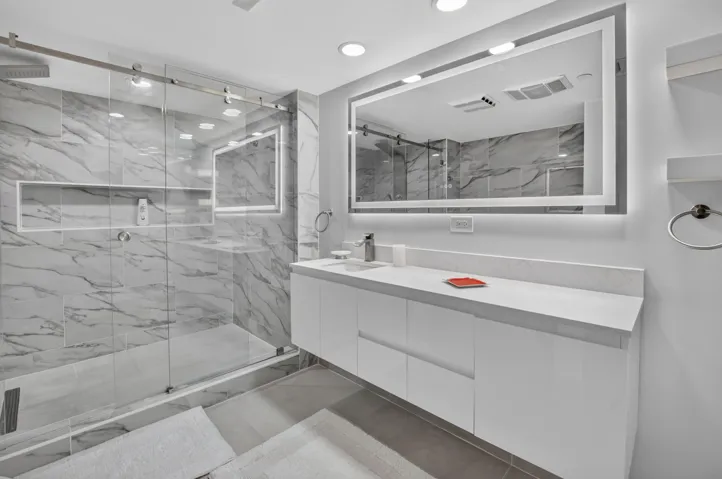 Modern bathroom featuring a frameless glass shower enclosure, a full-length vanity with integrated storage, and a large illuminated mirror