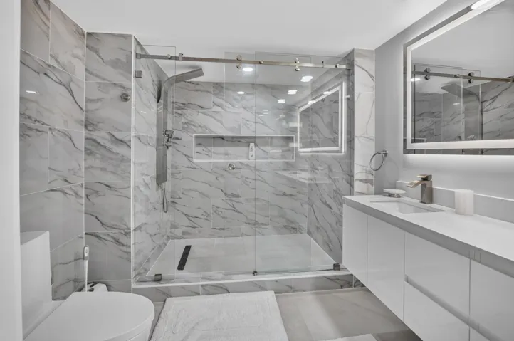 Large format marble-look tile, frameless glass shower enclosure, integrated shower niche, modern vanity with integrated sink, and illuminated mirror