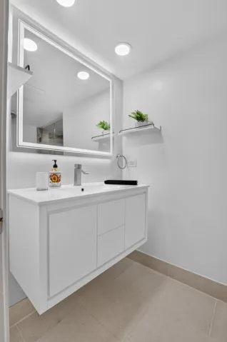 Floating vanity with an integrated sink and brushed chrome faucet, illuminated by a backlit mirror