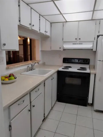 White cabinetry with silver hardware, light-toned countertops, white tile flooring, a black and white electric range, and a white refrigerator