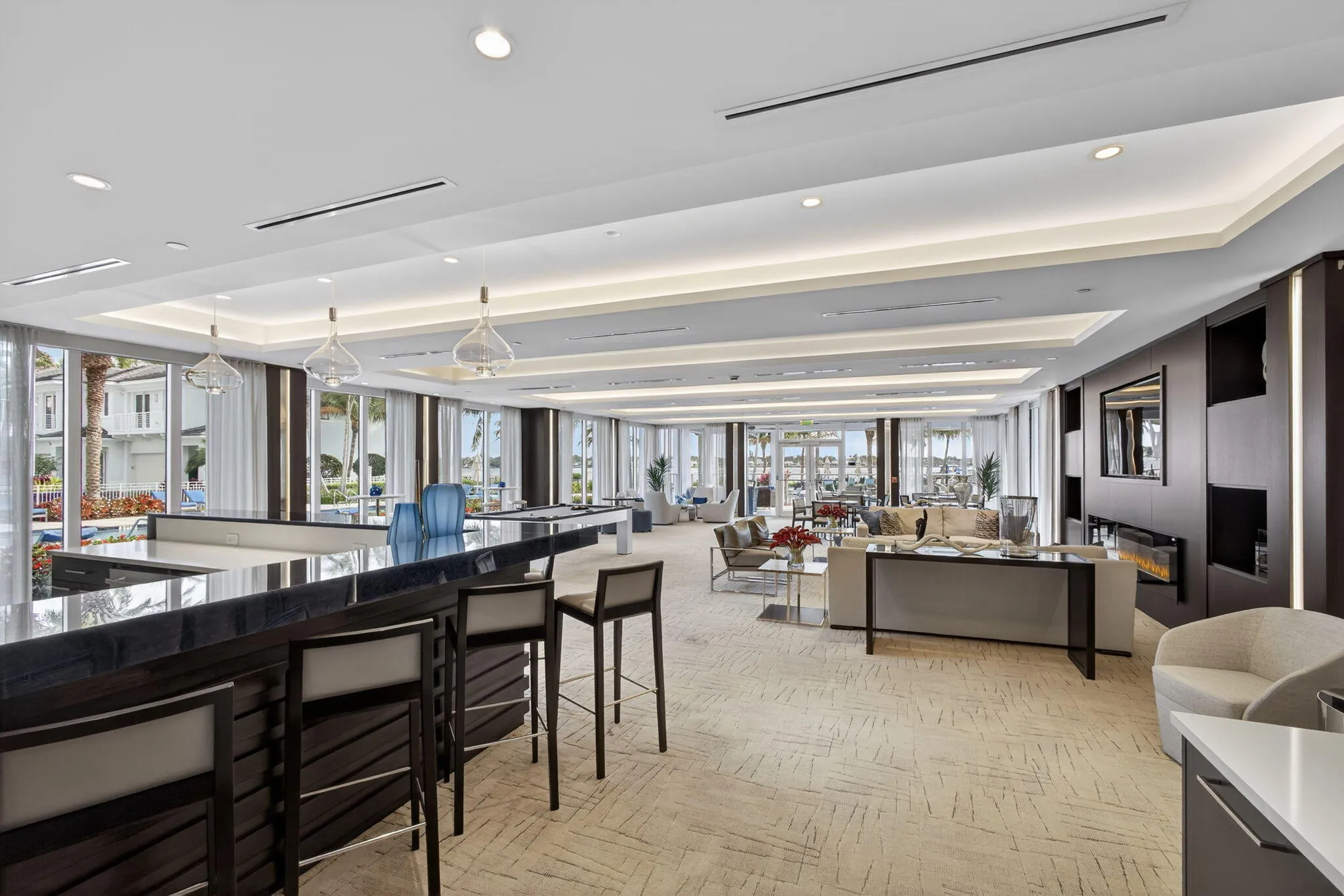 Expansive common area featuring a dark wood bar with a stone countertop, recessed and cove ceiling lighting, and large windows with sheer drapery
