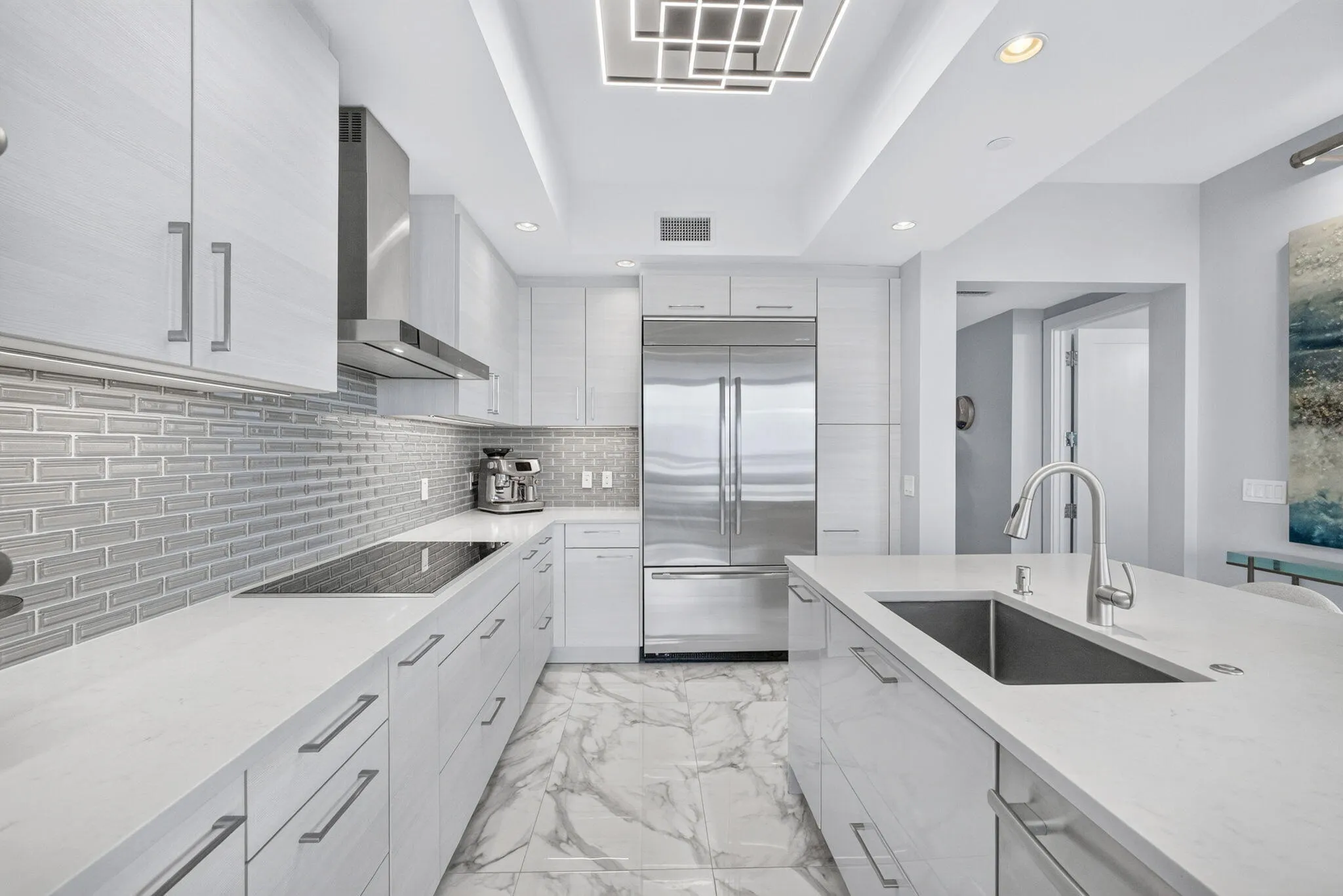 Large Open Concept Gourmet kitchen featuring a built-in cooktop, stainless steel High end appliances, a kitchen island with an undermount sink, a custom subway tile backsplash, and marble-finish flooring