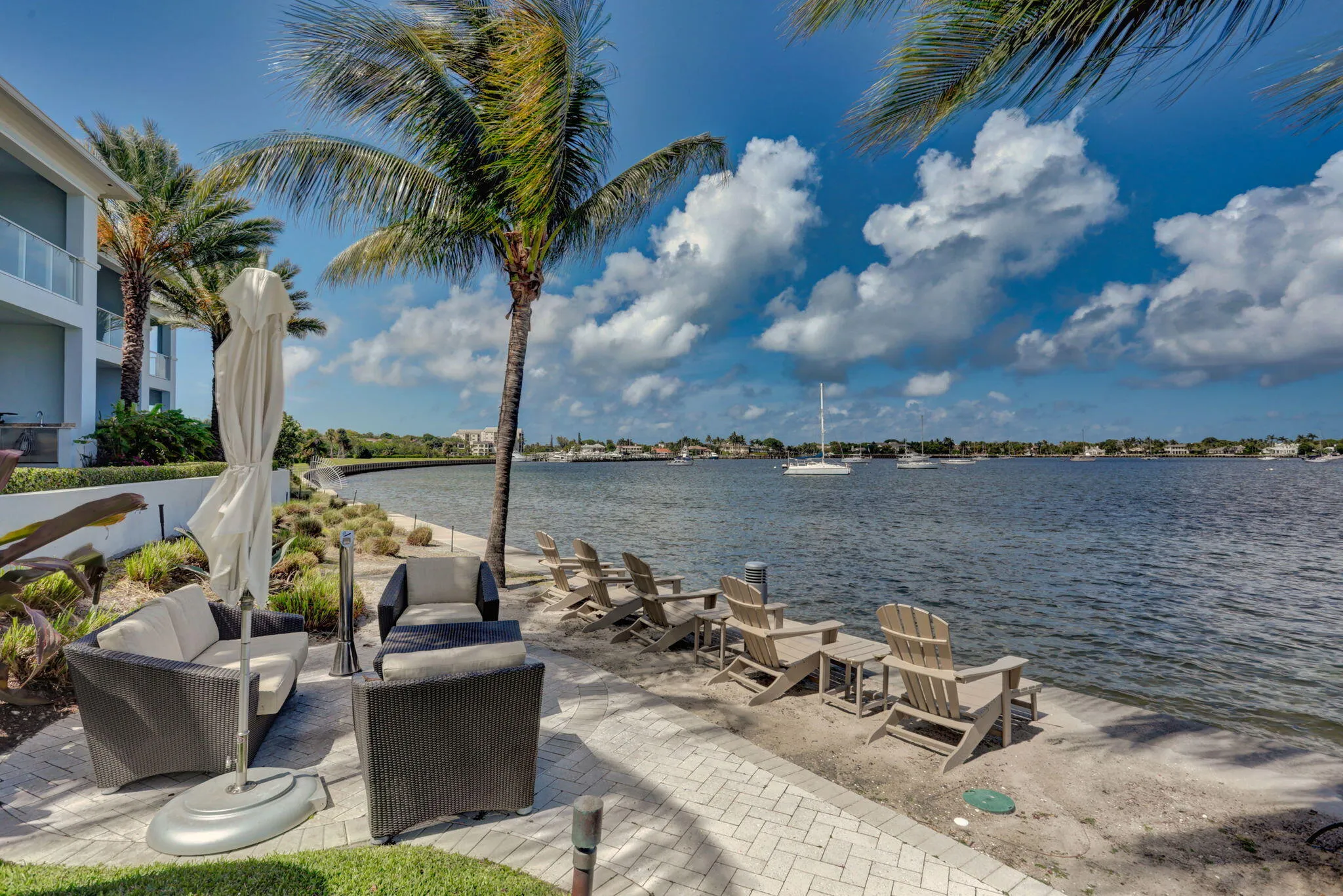 Waterfront property with a paver patio, lush landscaping, and mature palm trees