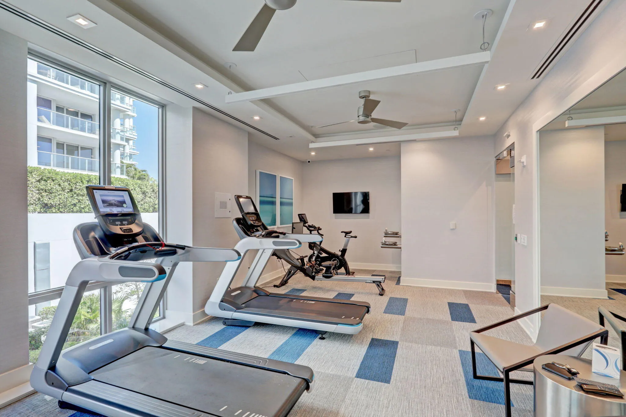Floor-to-ceiling window, ceiling fans, recessed lighting, wall-mounted television, and patterned carpet flooring