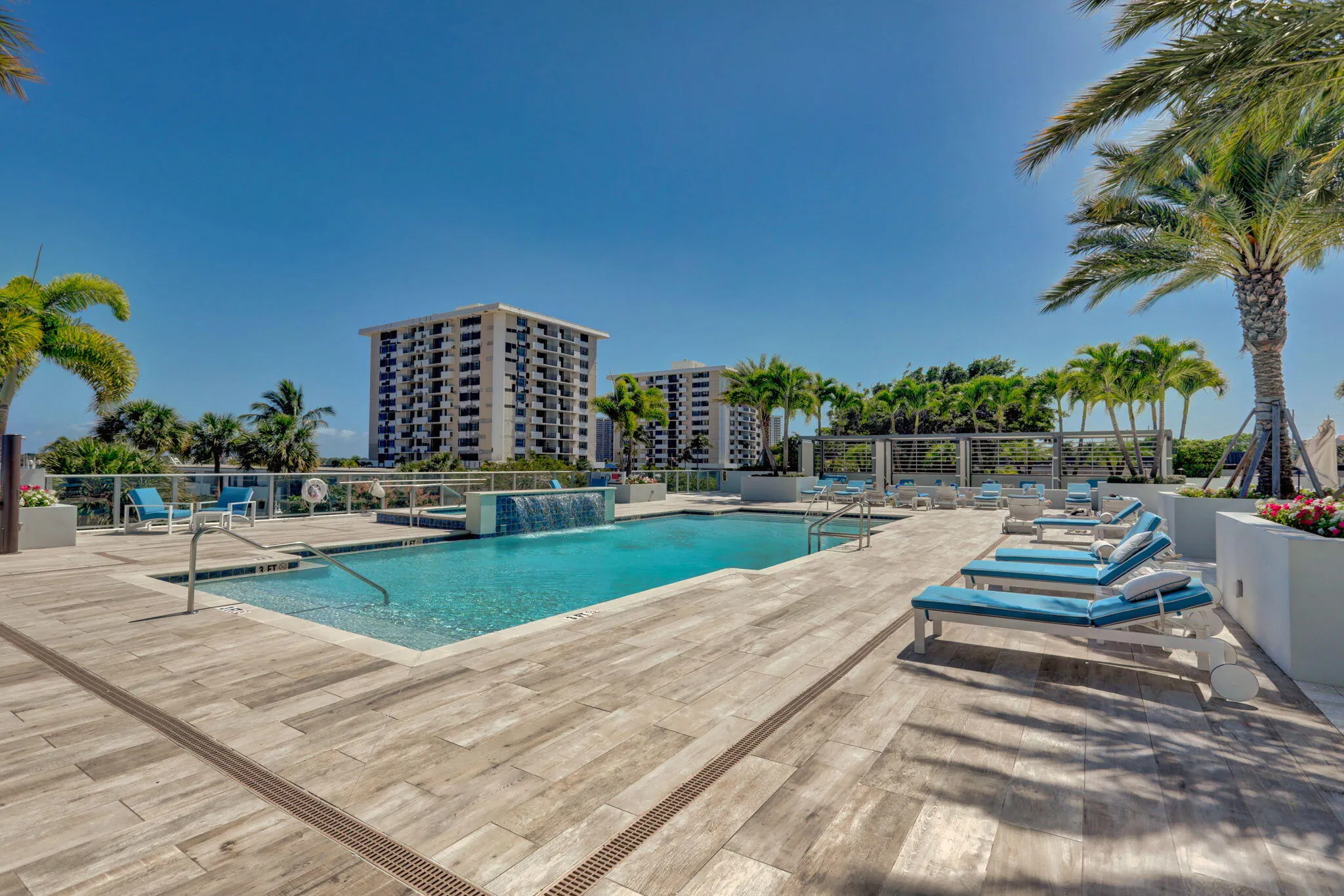 Swimming pool with an integrated waterfall feature, surrounded by a wood-finish deck and mature palm trees