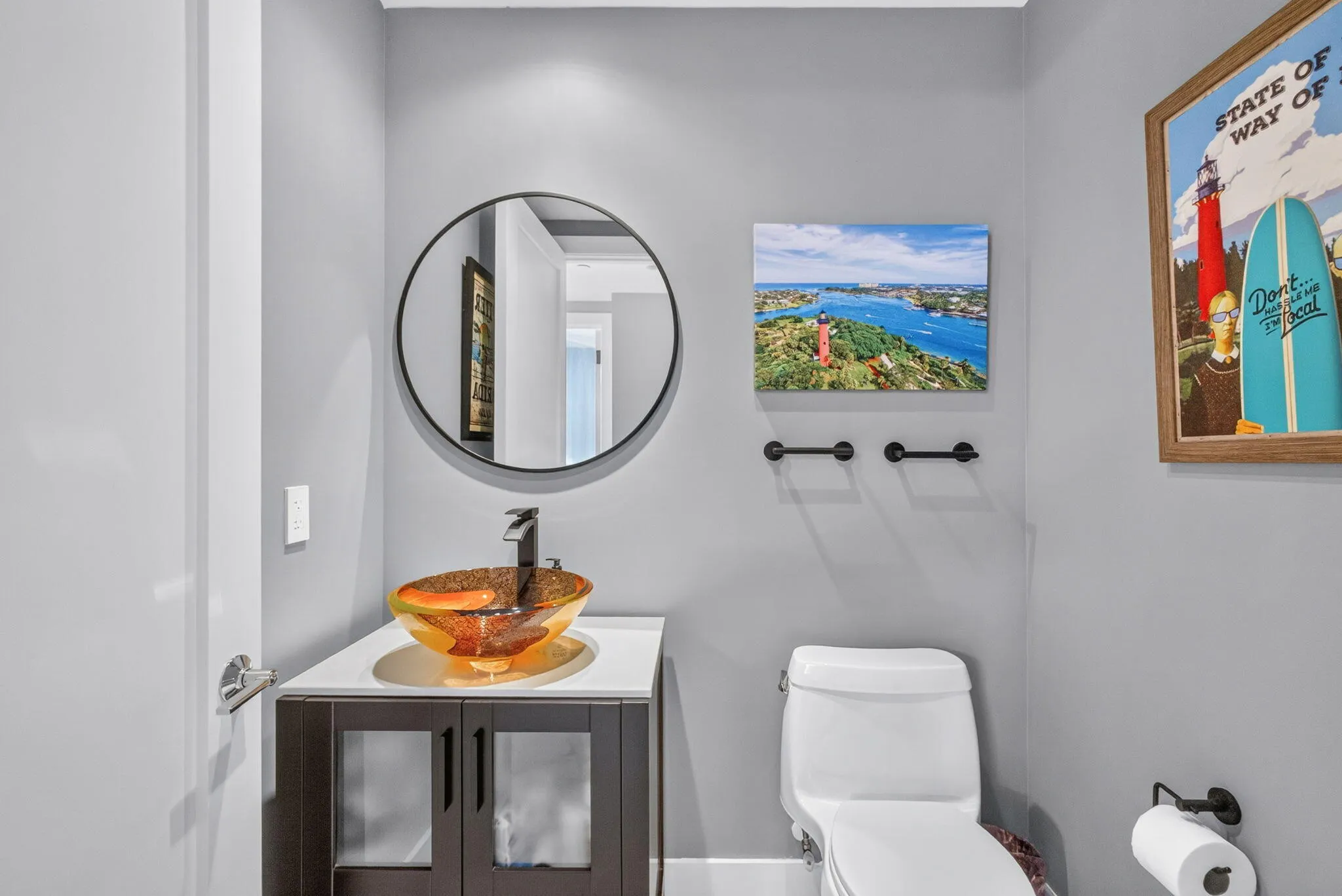 Wall-mounted circular mirror, vessel sink with dark faucet, dark wood-finish vanity with lower cabinetry, and white toilet