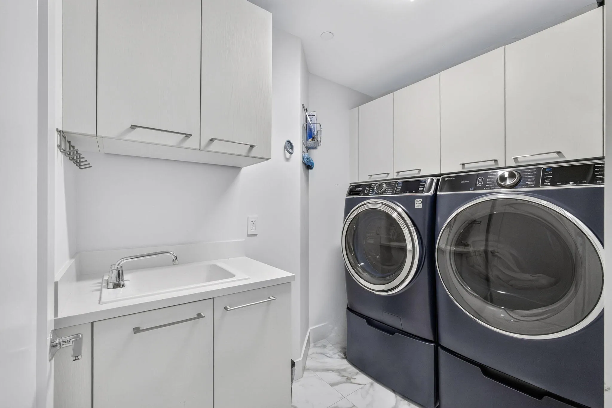 Convenient Laundry area with white cabinetry, a utility sink, and stone-finish flooring. Recently purchased upgraded appliances.