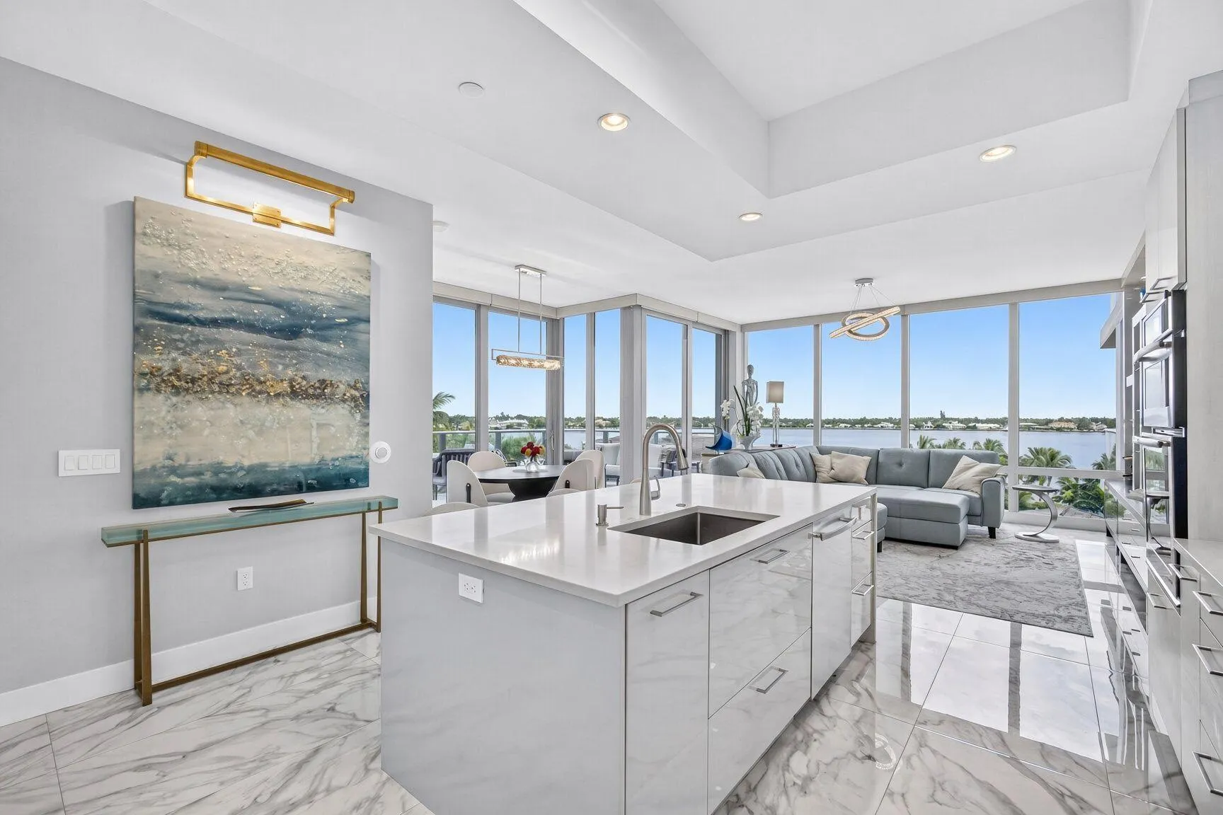 Open-concept living space with expansive floor-to-ceiling windows, a large kitchen island with an undermount sink, built-in ovens, and a coffered ceiling