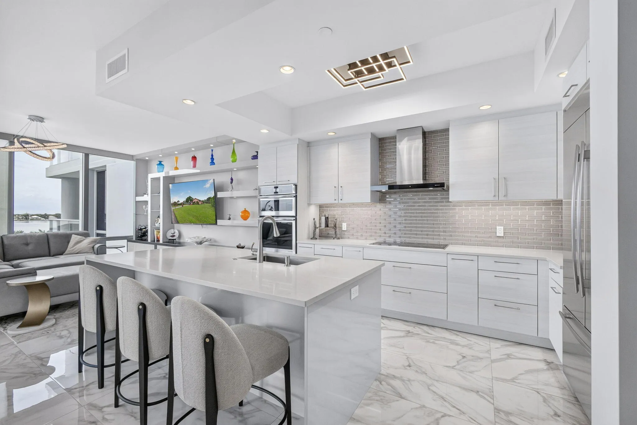 Spacious kitchen featuring an expansive island with seating, a sleek stainless steel range hood, built-in double ovens, and large format marble-look flooring