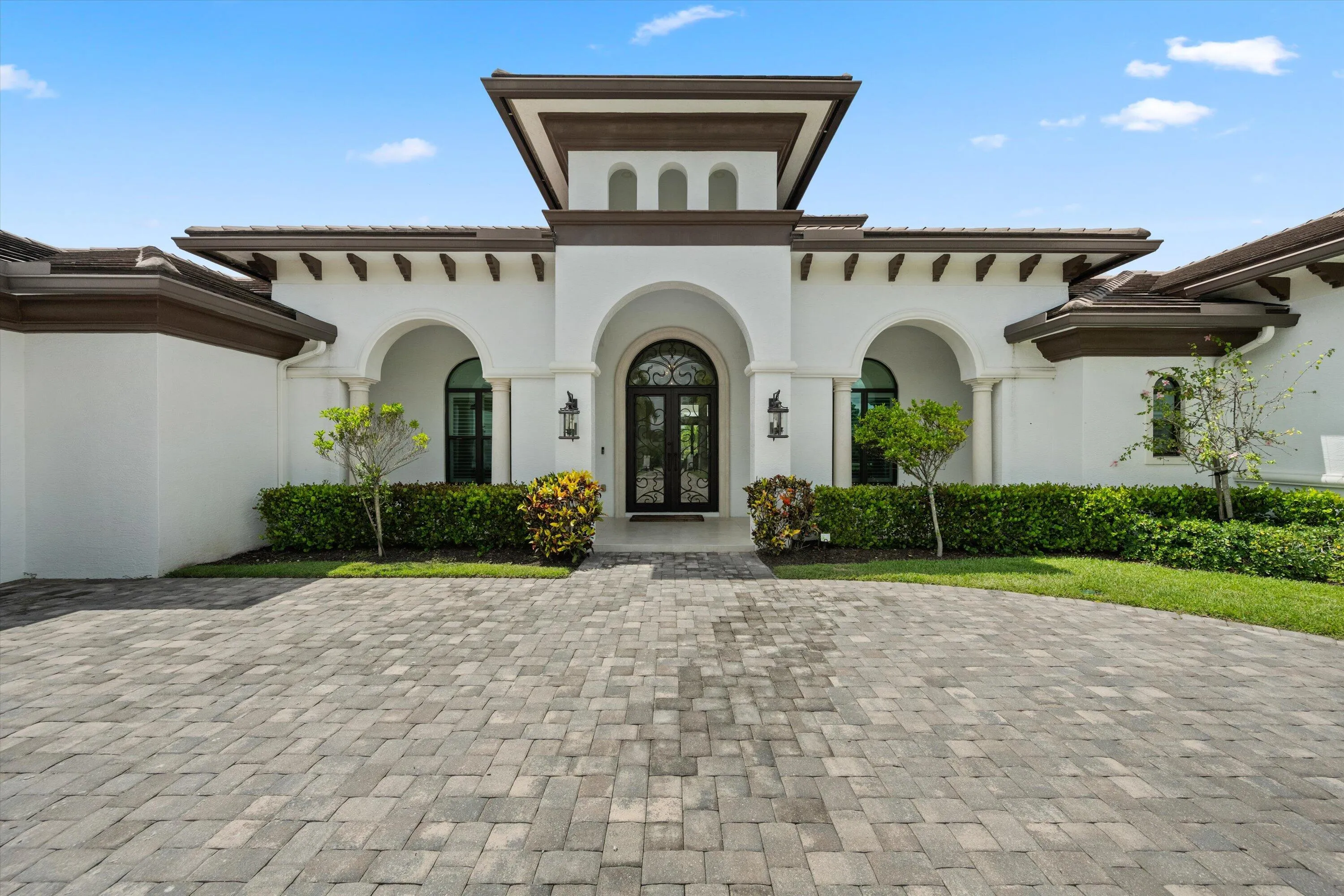 Stucco exterior with arched entryways, a paver driveway, and a central tower element