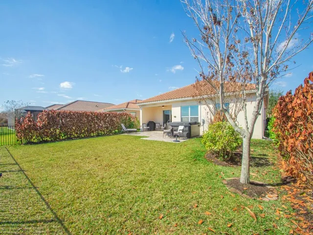 Rear exterior with a tiled roof, light-colored stucco siding, and a black wrought iron fence enclosing a grass lawn