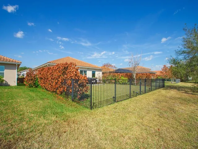 Rear exterior with a tiled roof, light-colored stucco siding, and a black wrought iron fence enclosing a grass lawn