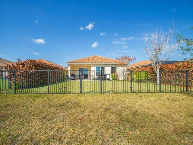 Rear exterior with a tiled roof, light-colored stucco siding, and a black wrought iron fence enclosing a grass lawn