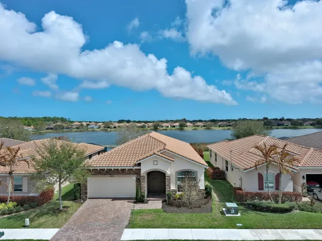 Mediterranean-style residence featuring a tile roof, paver driveway, manicured landscaping, and a waterfront location