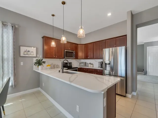 Modern kitchen featuring dark wood cabinetry, stainless steel appliances, a white stone-finish countertop, a tile backsplash, and recessed lighting