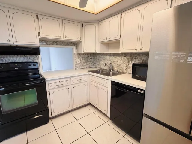 White cabinetry, square tile flooring, mosaic tile backsplash, double basin sink, and stainless steel refrigerator